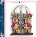 A wooden deer figurine stands in front of a Christmas tree, with two other deer figurines on either side. The deer are wearing red scarves and have antlers. The scene is set against a backdrop of a snowy landscape with pine trees.