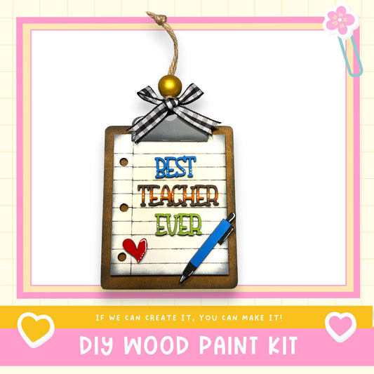 A DIY wood paint kit with a clipboard and a pen, featuring a heart-shaped charm and the text "BEST TEACHER EVER" on the clipboard.