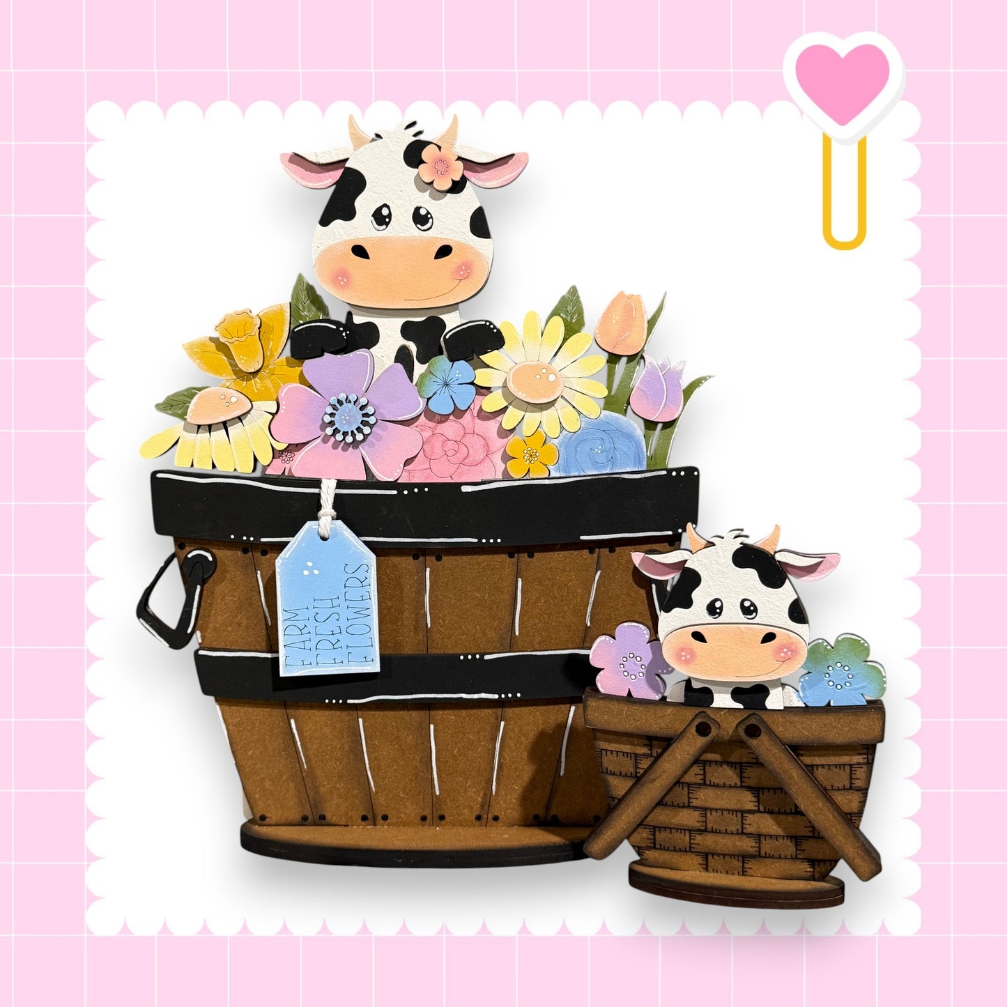 A wooden basket filled with colorful flowers and a smaller wooden basket with a cow inside, set against a pink background with a heart symbol.