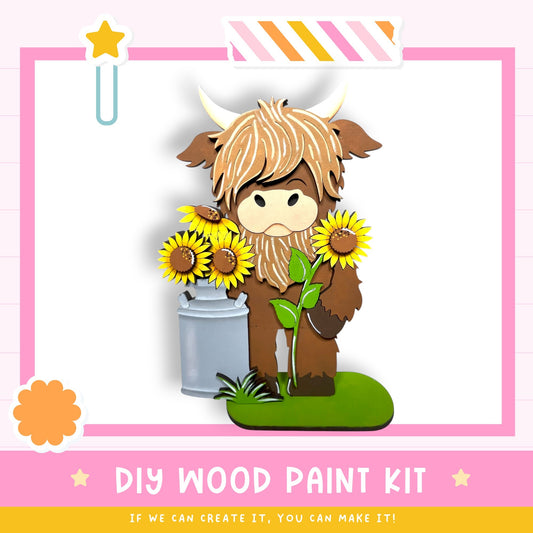 A wooden paint kit featuring a cartoon cow holding a vase of sunflowers and a plant, with a pink and white striped border and a star decoration.