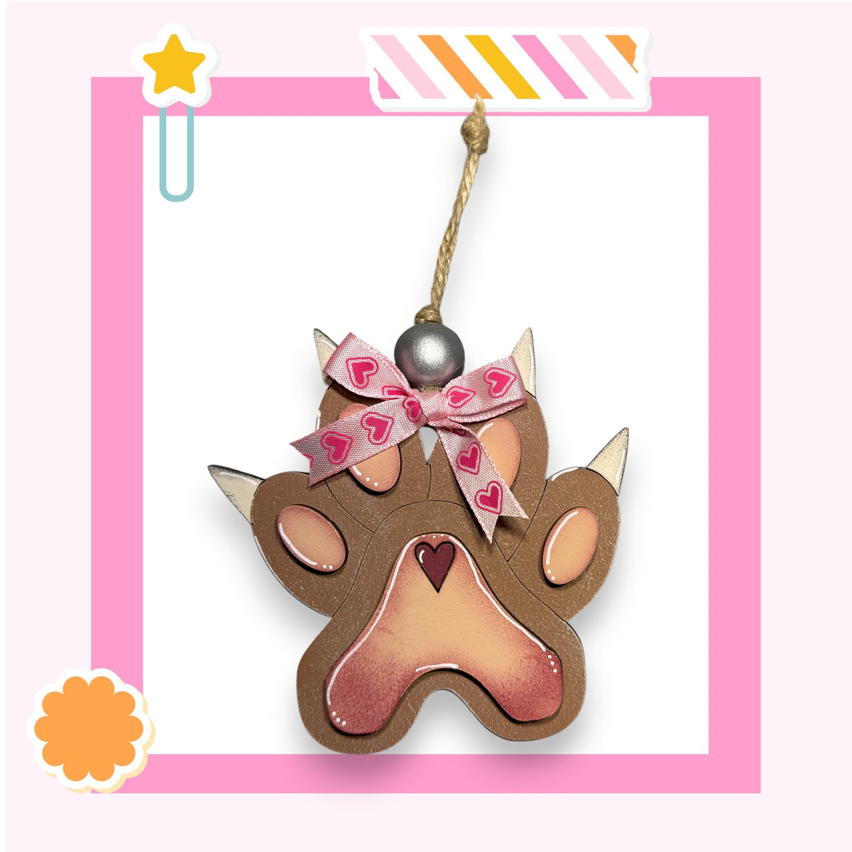 A brown paw print ornament with a heart-shaped ribbon and a star decoration, hanging from a string.