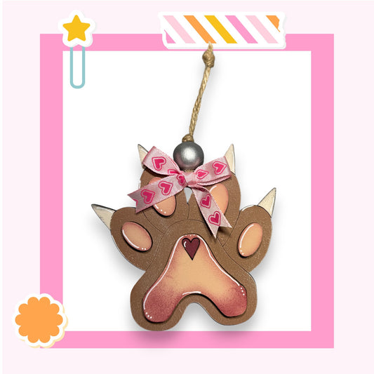 A brown paw print ornament with a heart-shaped ribbon and a star decoration, hanging from a string.