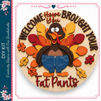A wooden sign with a turkey wearing blue jeans and surrounded by autumn leaves, with the text "Welcome Hope Brought Your Fat Pants" on it.