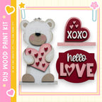 a wooden teddy bear holding a heart-shaped sign that says "XOXO" and another sign that says "Hello Love".