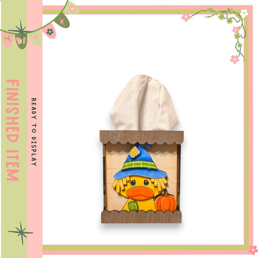 A wooden tissue box with a cartoon duck wearing a witch's hat and holding a pumpkin, set against a pink and green background.