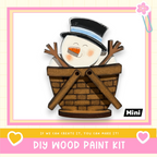 A wooden snowman figure sitting in a basket, with a caption that reads "If we can create it, you can make it!" and a DIY wood paint kit label.