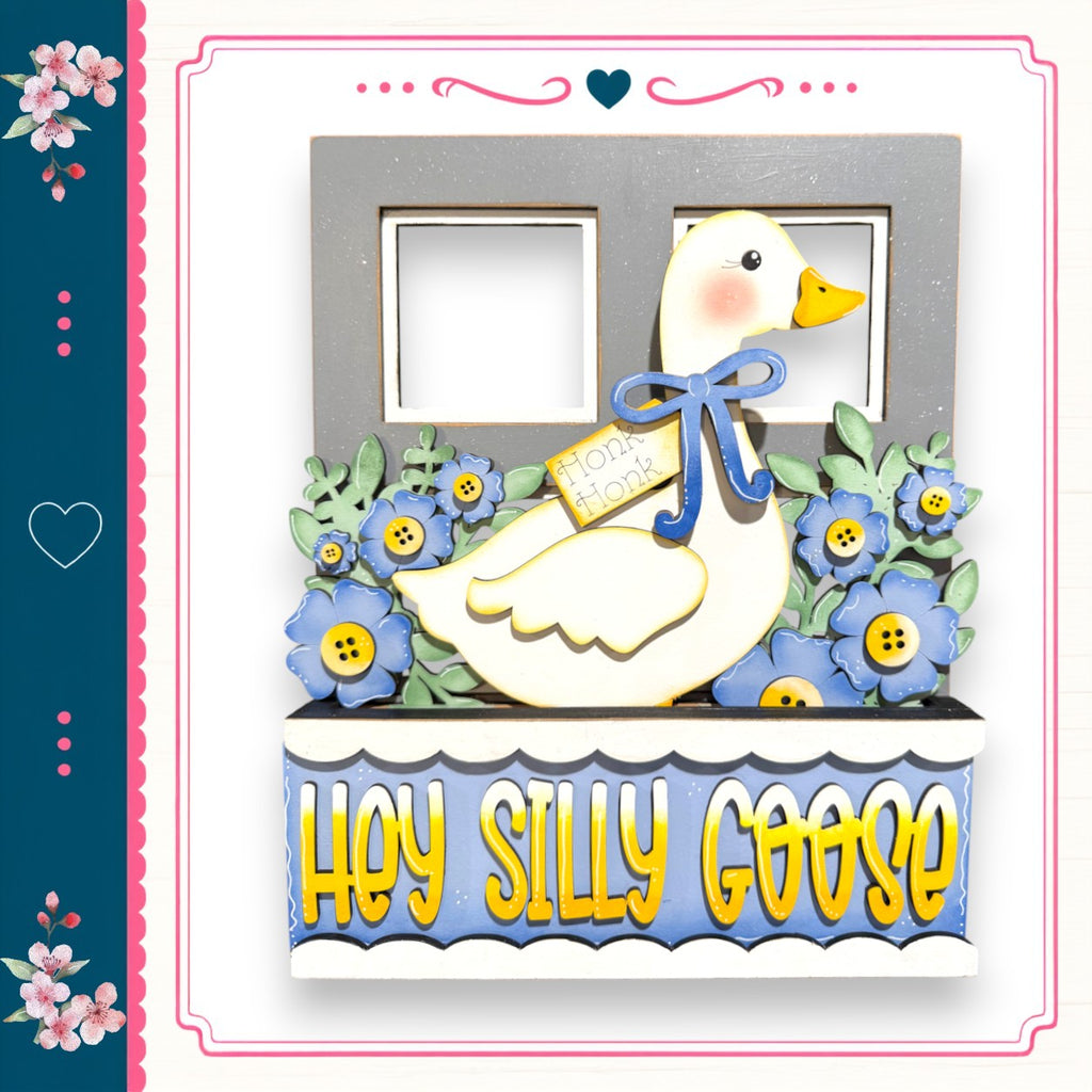 A decorative wooden frame with a cartoon goose and flowers, along with the text "Hey Silly Goose" written on it.