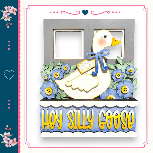 A decorative wooden frame with a cartoon goose and flowers, along with the text "Hey Silly Goose" written on it.