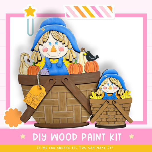 a DIY wood paint kit for creating a scarecrow, with two scarecrow figures sitting in wooden baskets. The kit includes a label and instructions for painting the scarecrow figures.