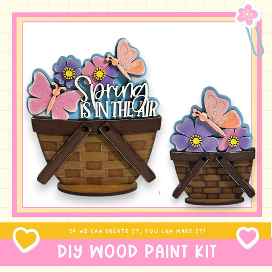 two wooden baskets filled with colorful flowers, including pink and purple flowers, and butterflies. The baskets are placed on a white background, and there is text at the bottom of the image that reads "DIY WOOD PAINT KIT" and "If we can create it, you can make it!"