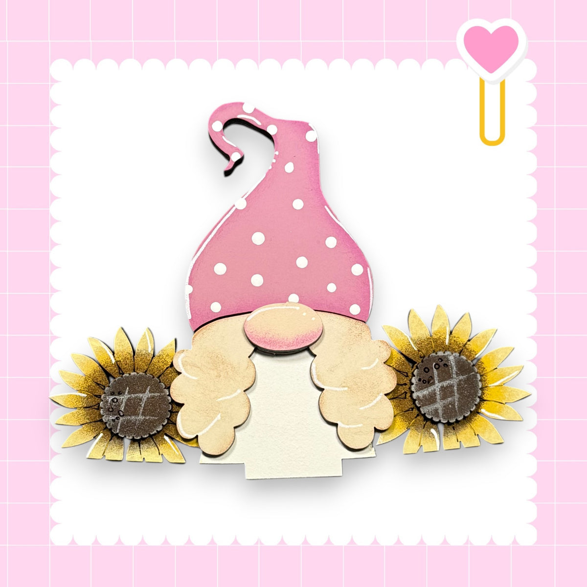 A pink polka dot hat with a gnome-like face and two sunflower-shaped buttons on either side, set against a pink background with a heart shape.