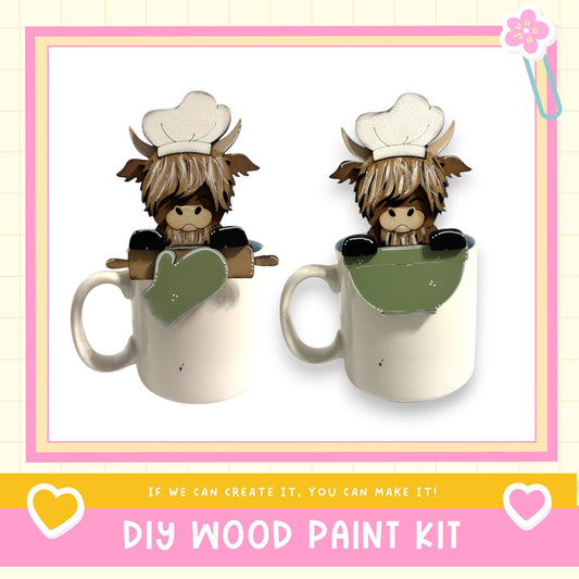 two ceramic mugs with wooden cutouts of cartoon cow characters wearing chef hats, sitting inside them. The mugs are placed against a white background, and there is text at the bottom of the image that reads "DIY WOOD PAINT KIT" and "IF WE CAN CREATE IT, YOU CAN MAKE IT!"