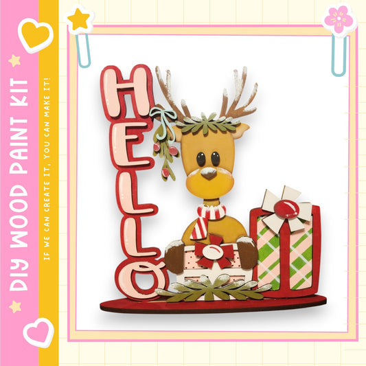 A wooden paint kit featuring a cartoon reindeer with antlers and a "Hello" sign, surrounded by wrapped presents and holiday decorations.