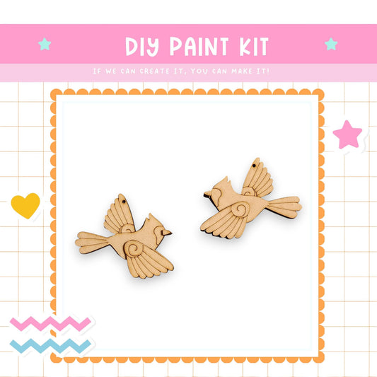 The image is a DIY paint kit featuring two wooden bird ornaments, with a pink and white border and decorative elements surrounding the frame.