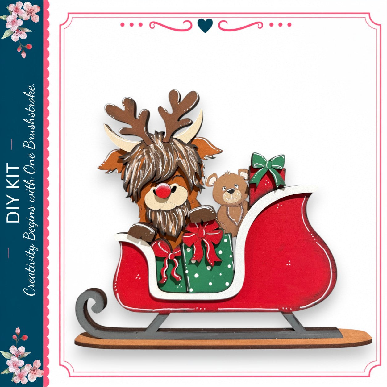 A wooden reindeer with antlers sits on a red sled, carrying a teddy bear and wrapped gifts, against a white background.