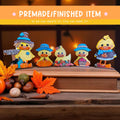 a group of five small, colorful duck figurines arranged on a wooden surface, with autumn leaves and other seasonal decorations in the background.