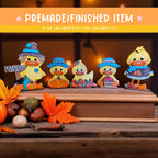 a group of five small, colorful duck figurines arranged on a wooden surface, with autumn leaves and other seasonal decorations in the background.