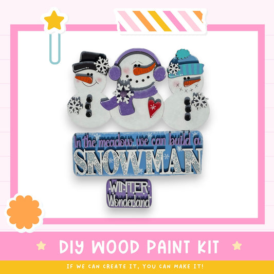 The image is a promotional poster for a DIY wood paint kit that allows users to create a snowman. It features three snowmen with various accessories, such as hats, scarves, and snowflakes, arranged in a visually appealing manner. The text on the poster encourages viewers to create their own snowman using the provided kit, emphasizing the fun and creativity involved in the process.