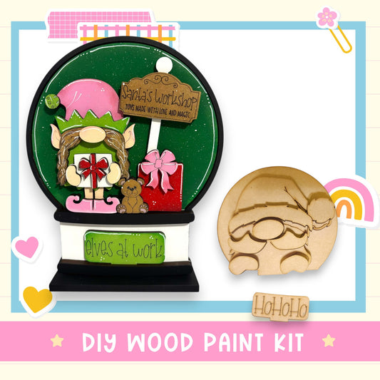 a DIY wood paint kit for creating a Christmas ornament, including a snow globe and a Santa Claus-themed cutout.