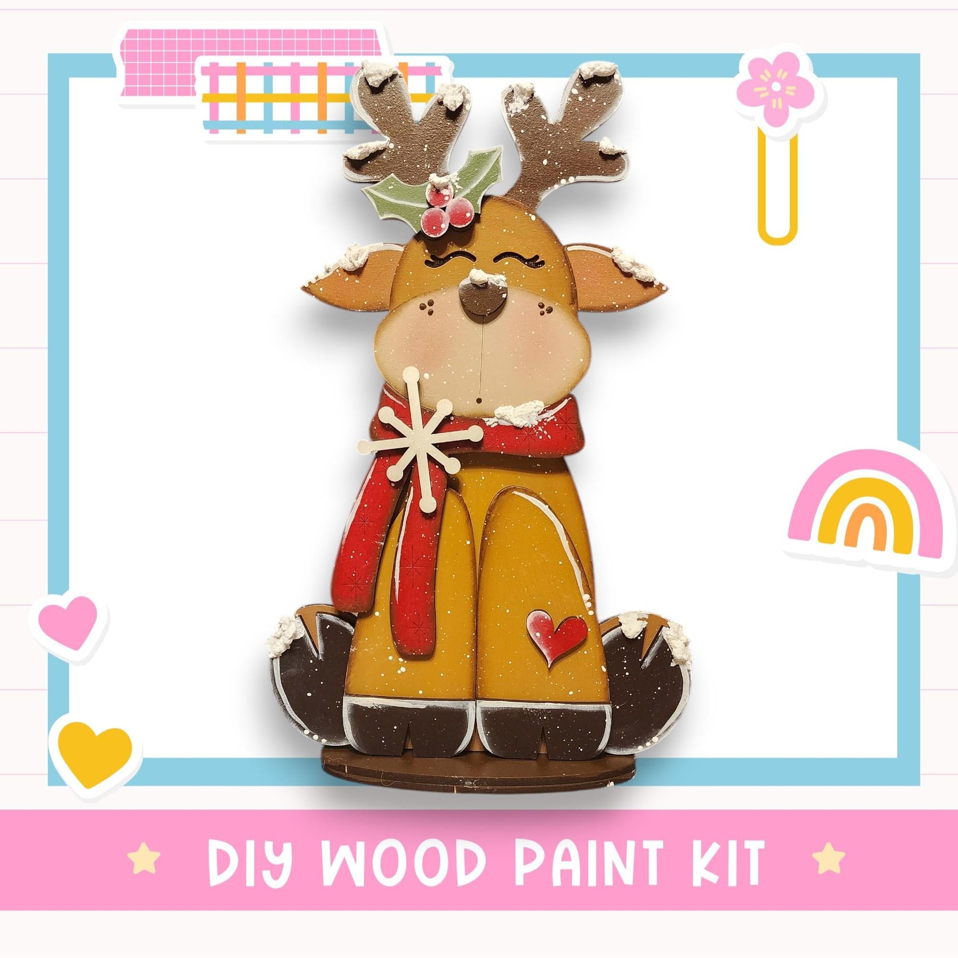 A wooden reindeer figure with antlers and a red scarf, sitting on a wooden base, is the central focus of the image. The background includes various colorful stickers and a rainbow, creating a festive and whimsical atmosphere. The text "DIY WOOD PAINT KIT" is prominently displayed, indicating that this is a DIY wood paint kit for creating a wooden reindeer figure.