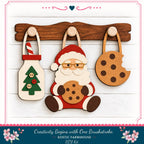 A DIY kit for creating a rustic farmhouse-style decoration featuring a wooden Santa Claus figure holding a cookie, a Christmas tree, and a cookie with a bite taken out of it.