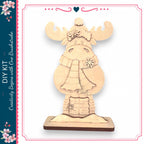 A wooden snowman decoration with antlers and a scarf, sitting on a wooden base.