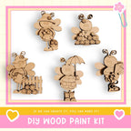 The image is a DIY wood paint kit featuring five wooden bee figurines in various poses, including one holding an umbrella.