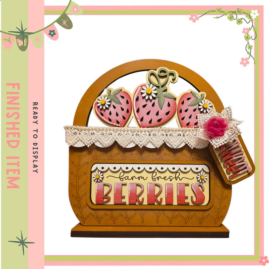 A wooden basket with a lace trim, decorated with a sign that says "Farm Fresh Berries". The basket is filled with strawberries, and there is a rose attached to it. The image is a decorative piece, likely used for display or as a gift.