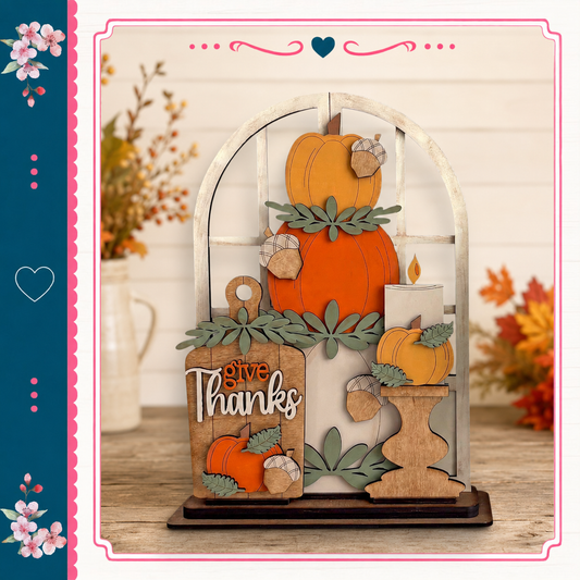 A wooden display with a carved pumpkin and acorns, featuring the text "Give Thanks" in a decorative font. The display is set against a backdrop of autumn foliage and flowers, creating a festive and seasonal atmosphere.