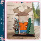 A wooden toy moose holding fishing gear, including a fishing rod and a small fish, is displayed on a wooden surface.