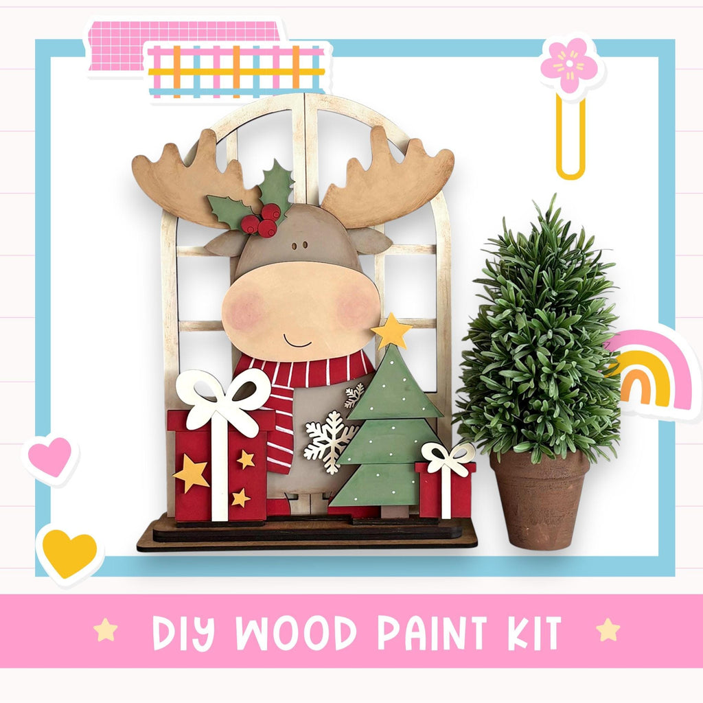 a DIY wood paint kit for creating a wooden ornament resembling a moose or deer, with a Christmas tree and presents.