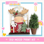 a DIY wood paint kit for creating a wooden ornament resembling a moose or deer, with a Christmas tree and presents.
