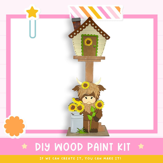 a wooden birdhouse with a cow figurine inside, surrounded by sunflowers. The image is a collage of various elements, including a star, a flower, and a cow. The text "DIY WOOD PAINT KIT" is displayed, along with the phrase "If we can create it, you can make it!"