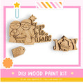The image is a DIY wood paint kit featuring a nativity scene with a baby in a manger, a wooden sign with the phrase "Joy to the World", and a wooden tag that says "O Holy Night".