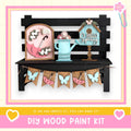 a DIY wood paint kit for creating a spring-themed decoration, including a wooden bench with a pink umbrella, a blue watering can, and a birdhouse. The kit is designed to allow users to create their own spring-themed decorations.