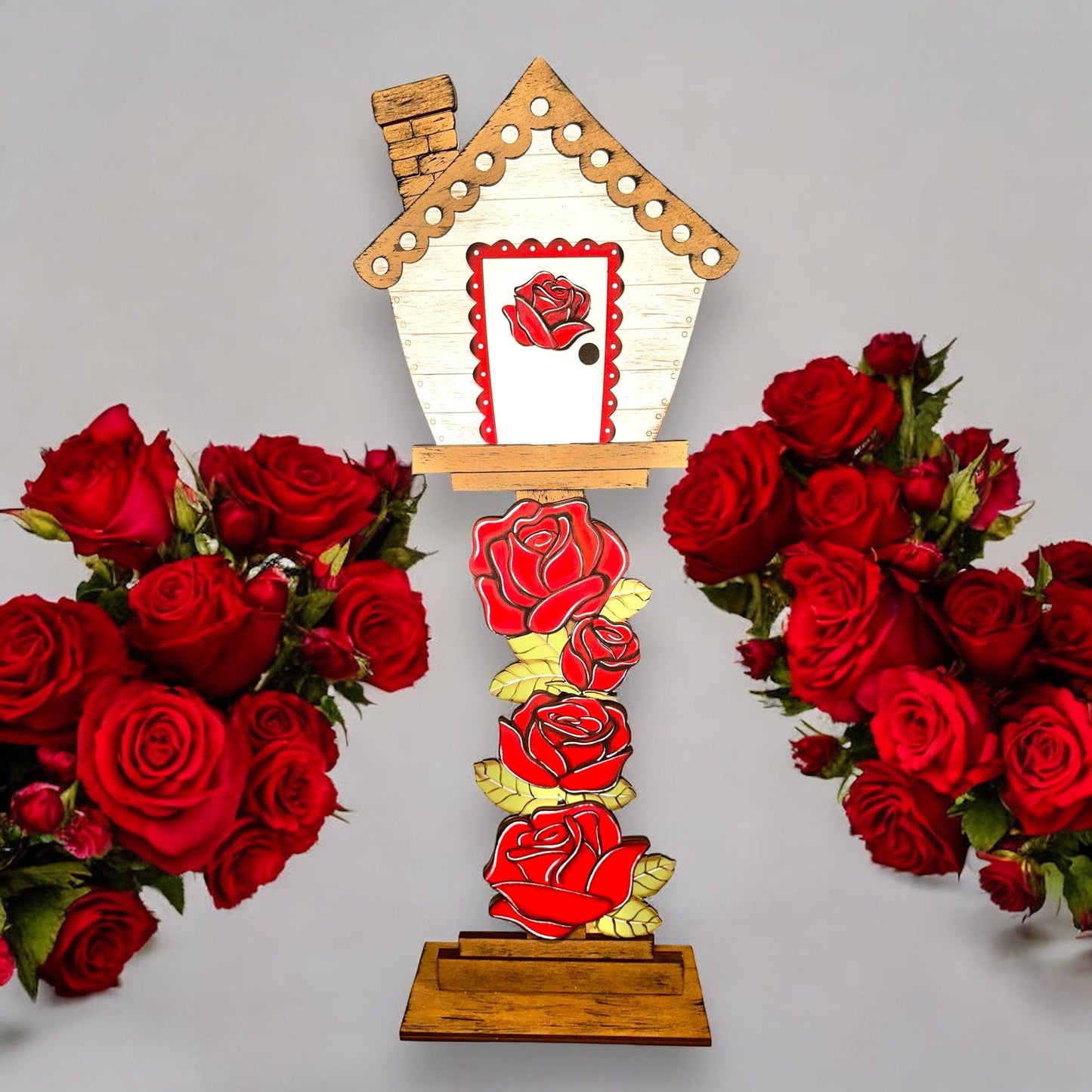 a clock with a house on top of it surrounded by red roses