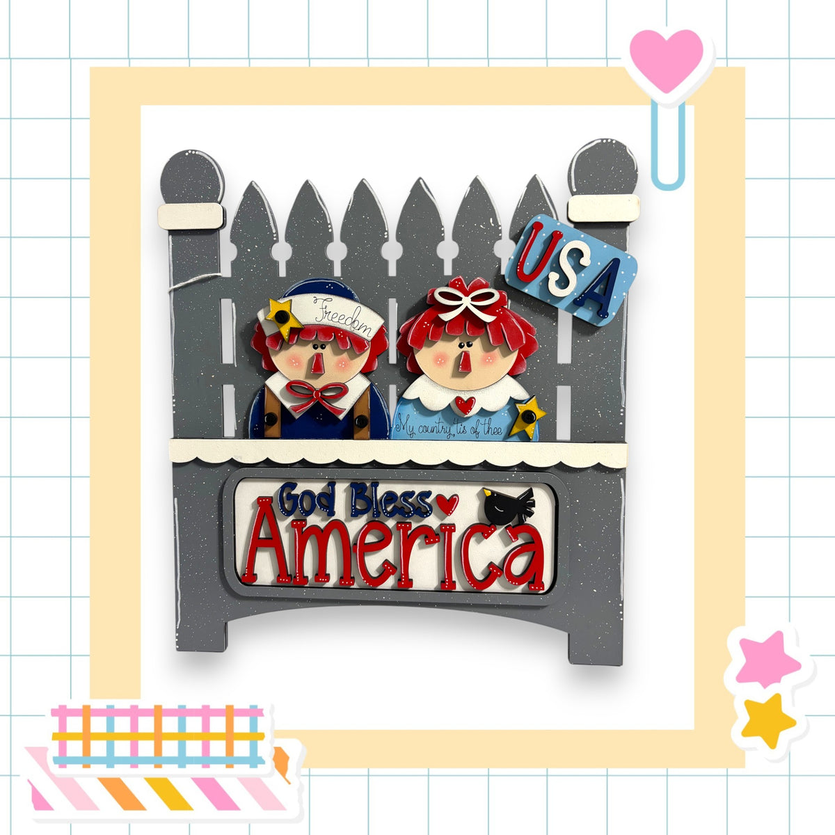 A decorative wooden sign with two cartoon-like figures, one wearing a blue shirt and the other a red shirt, sitting on a wooden bench. The sign has the text "God Bless America" written on it.