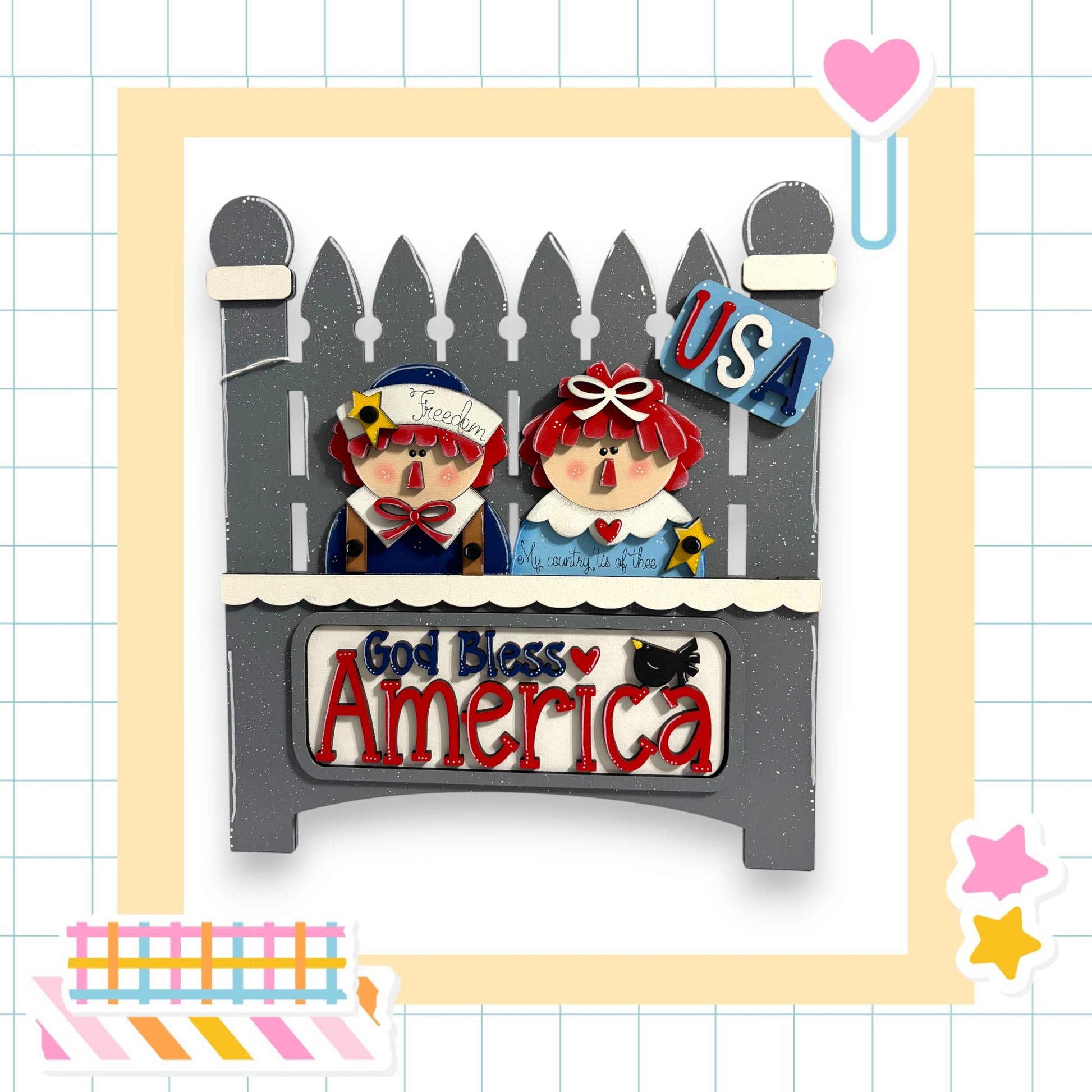 A decorative wooden sign with two cartoon-like figures, one wearing a blue shirt and the other a red shirt, sitting on a wooden bench. The sign has the text "God Bless America" written on it.