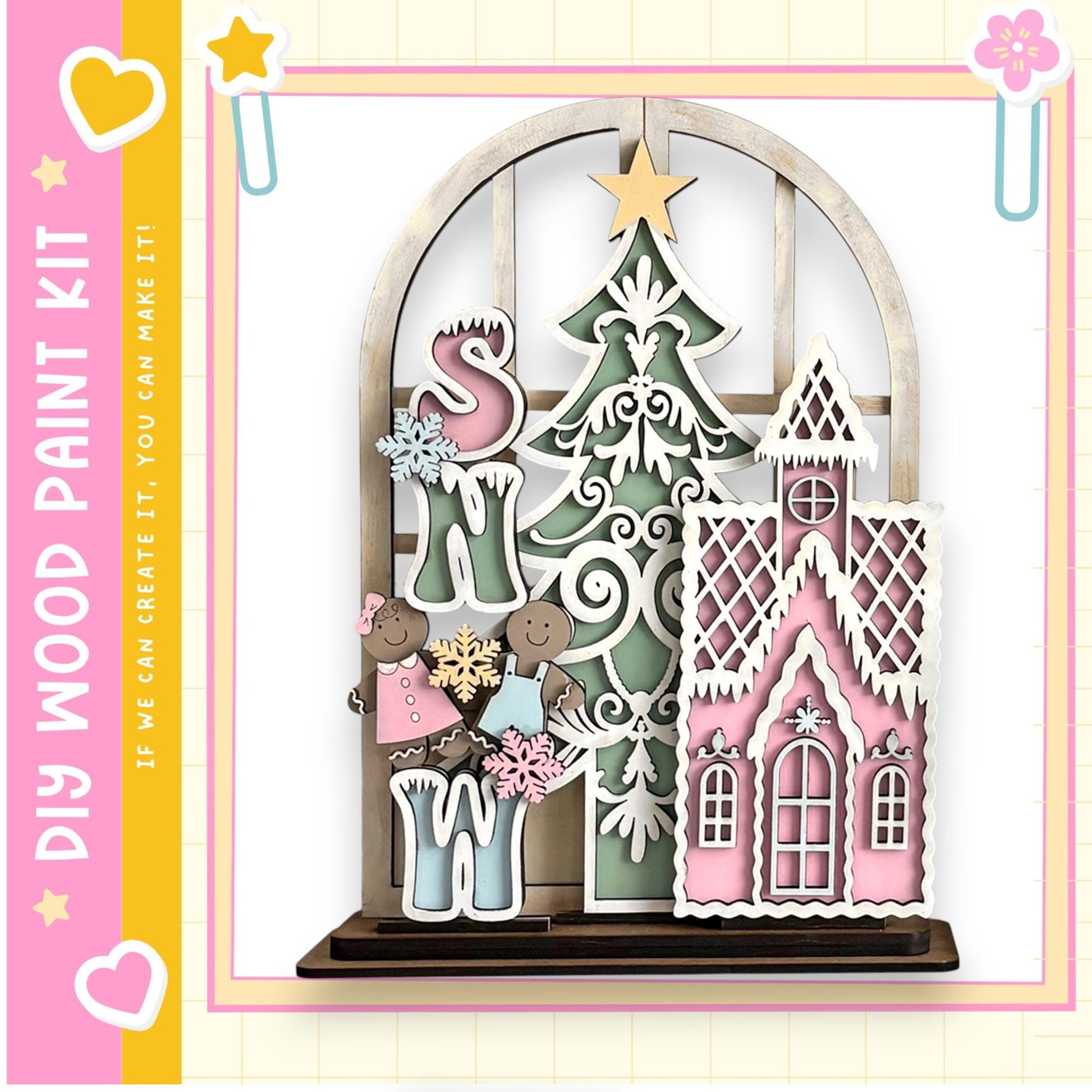 A wooden Christmas tree with a pink roof and a small pink house with a white roof, along with a pair of children holding snowflakes. The image is framed by a pink border with a yellow star and a pink heart.