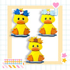 three yellow duck figures with different accessories, such as bows and baseballs, arranged in a frame.