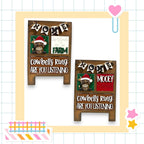 two wooden signs with text and illustrations, including a cowbell and a moose, set against a background with a grid pattern.
