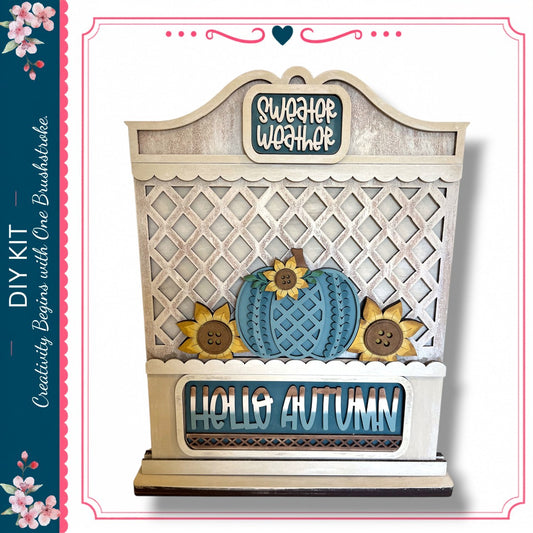 a decorative wooden sign with a lattice pattern, a blue pumpkin, and sunflowers, along with the text "Hello Autumn".