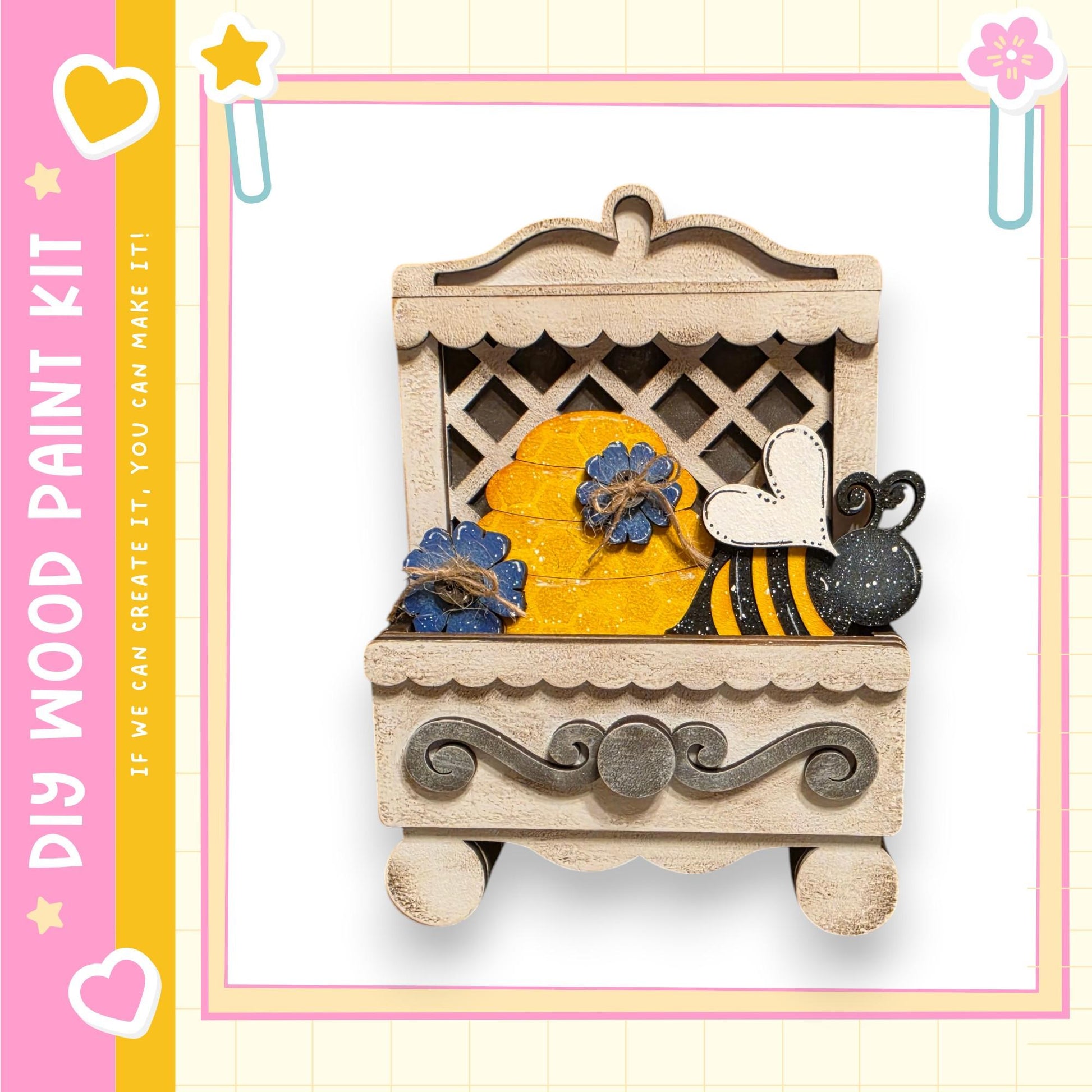 A wooden paint kit featuring a decorative wooden bee and a honeycomb-like structure, with a heart and star motif on the border.