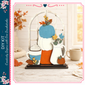 A DIY kit featuring a wooden frame with a pumpkin, a teapot, and a vase, set against a backdrop of autumn leaves and flowers.