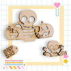 a Halloween-themed collage with various wooden cutouts, including a skeleton holding a carved pumpkin, a smaller carved pumpkin, and a carved pumpkin. The collage is set against a grid background with a heart and a star decoration.