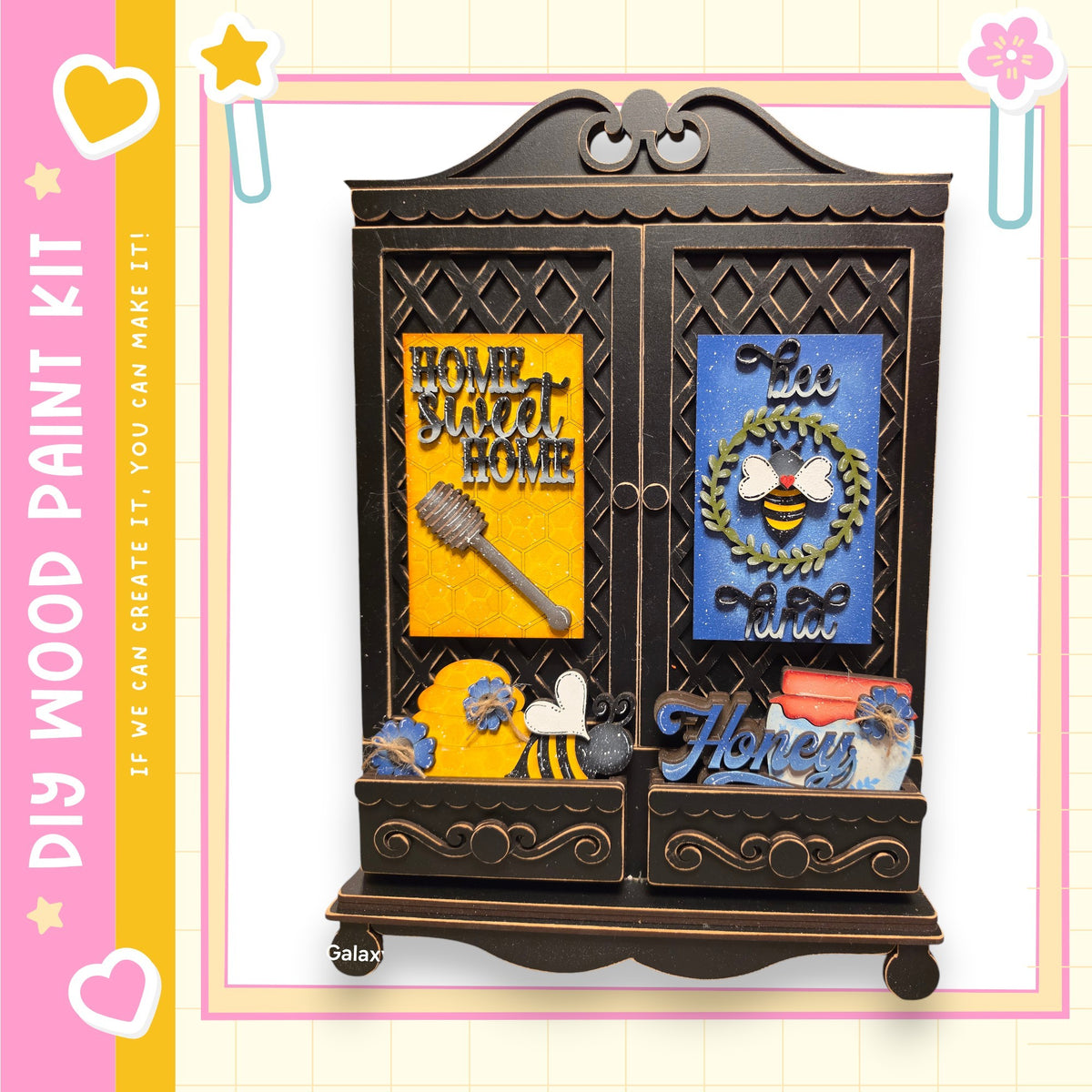 The image is a wooden paint kit featuring a decorative cabinet with various items, including a bee, a honey jar, and a wreath.