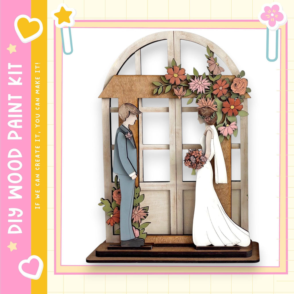 A wooden wedding cake topper depicting a bride and groom standing in front of a floral arch.