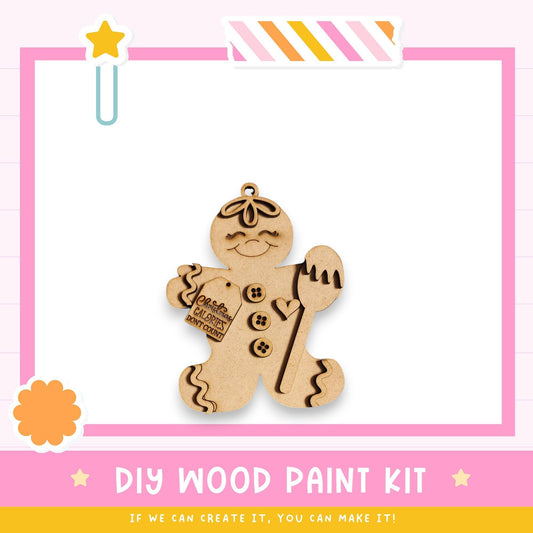a DIY wood paint kit, with a wooden gingerbread man figure as the main focus. The kit appears to be made of wood and is displayed against a pink and white background.
