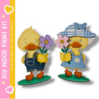 two cartoon duck figures holding flowers, standing on a green base.