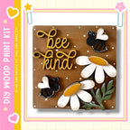 The image is a wooden paint kit featuring a decorative design with a bee and flowers. The kit includes a wooden board with the words "bee kind" written on it, along with bee and flower cutouts. The kit appears to be a creative project for children, as indicated by the "DIY" label.